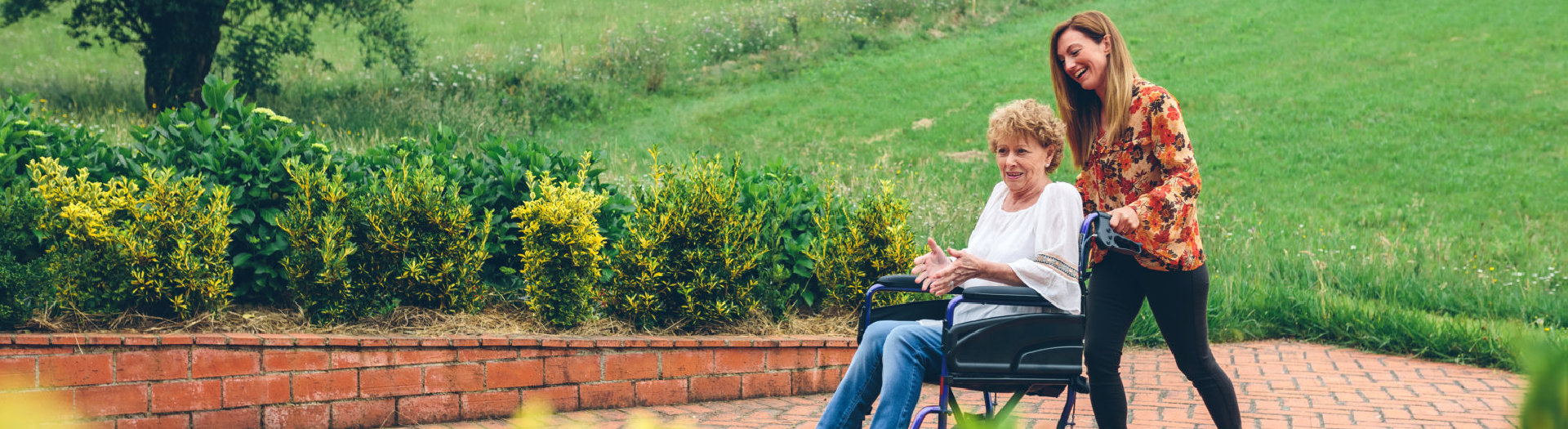 Young women carrying her mother in a wheelchair through the garden